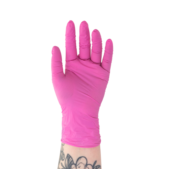 Une main portant un gant en nitrile rose Killer Beauty (boîte de 100) est levée sur fond blanc, laissant apparaître partiellement un tatouage floral au poignet.